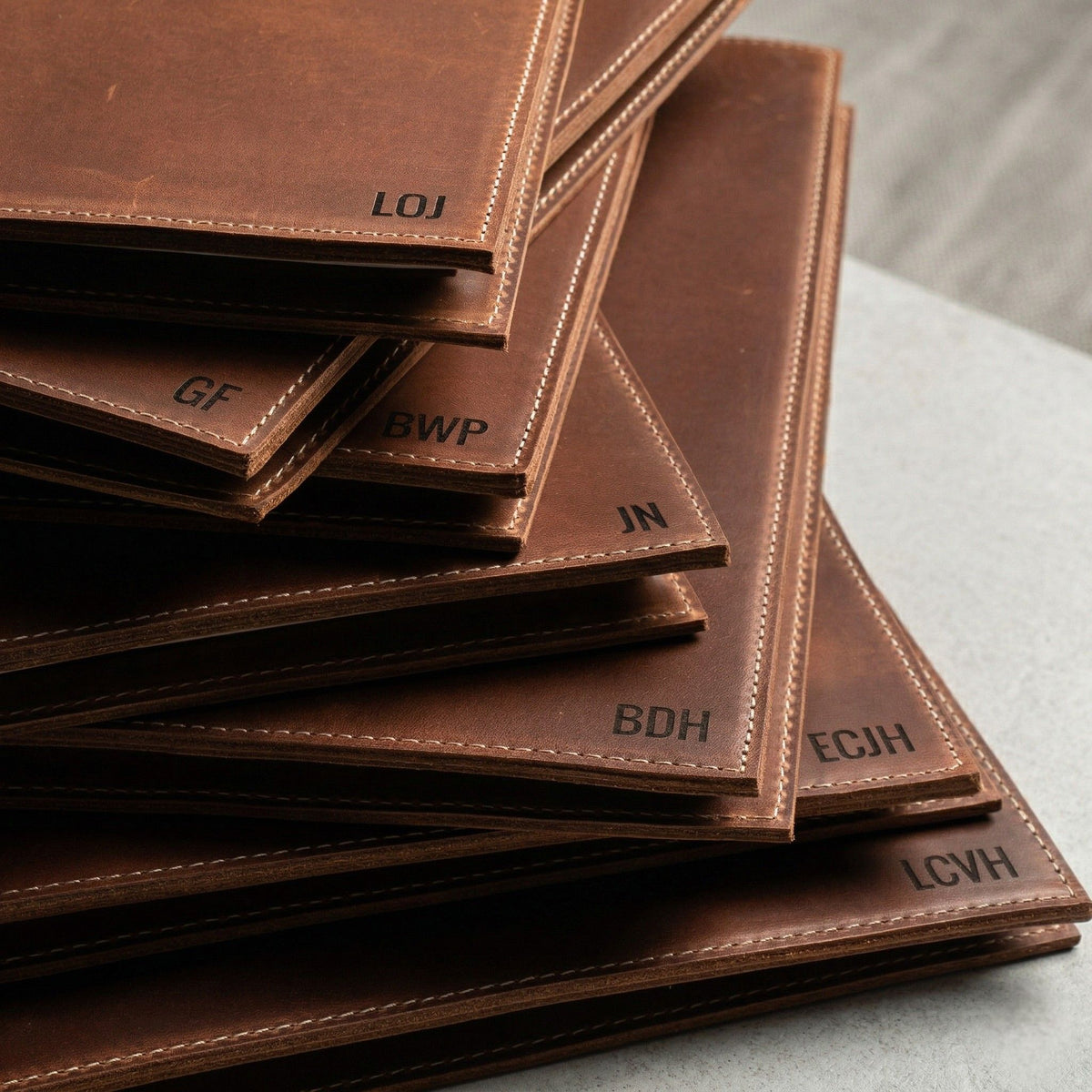 Stack of brown leather padfolios, each personalized with a name